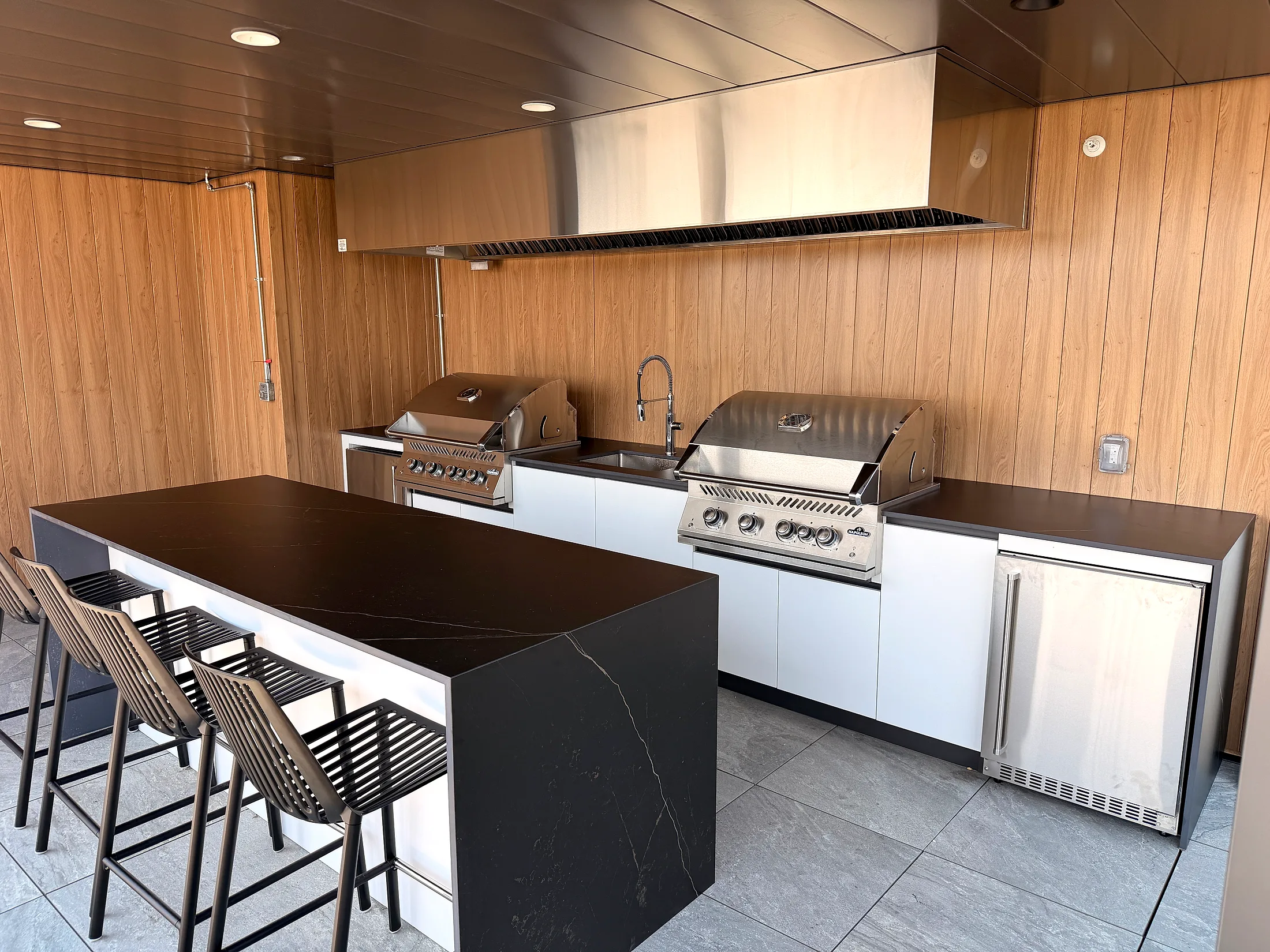 Commercial outdoor kitchen on a building’s rooftop terrace in Quebec City, with a double cooking line, Orastone Midnight island, and Snow White cabinets