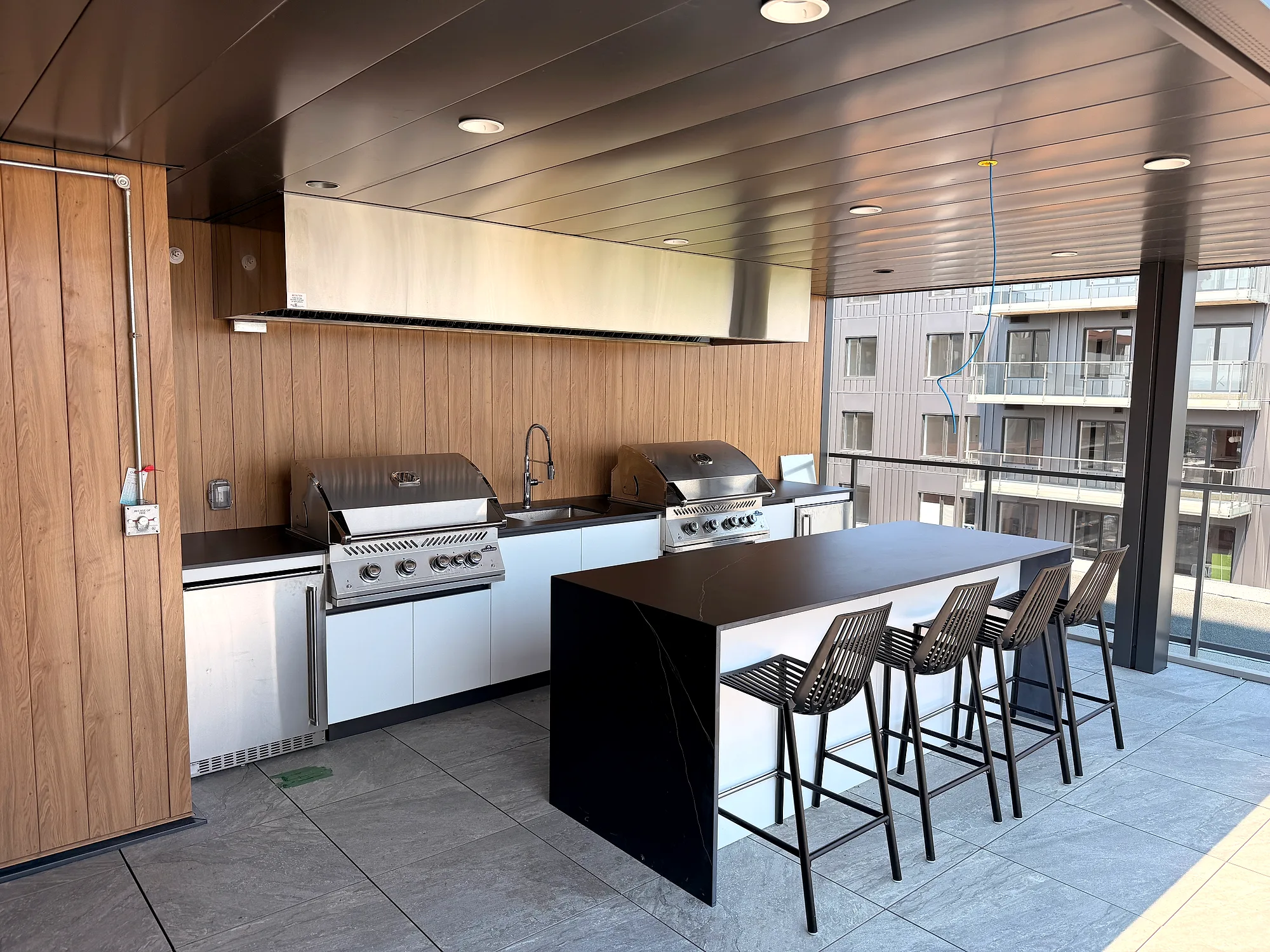 Vue d’ensemble de la cuisine commune avec deux BBQ Napoléon, îlot bar et tabourets, projet Place Fleur de Lys à Québec