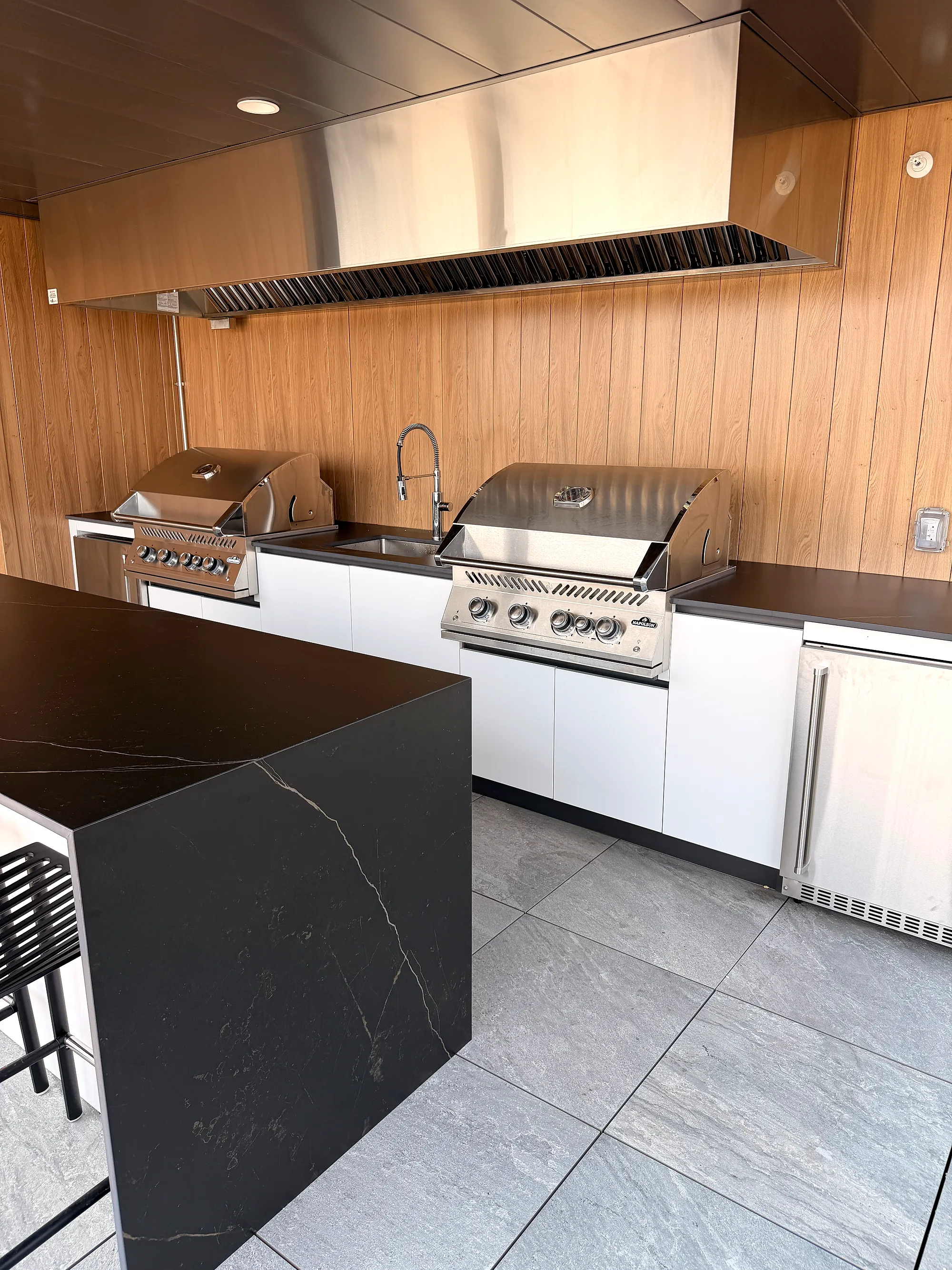 Ligne de cuisson avec deux BBQ Napoléon série 700, évier et hotte en inox sous parois de bois