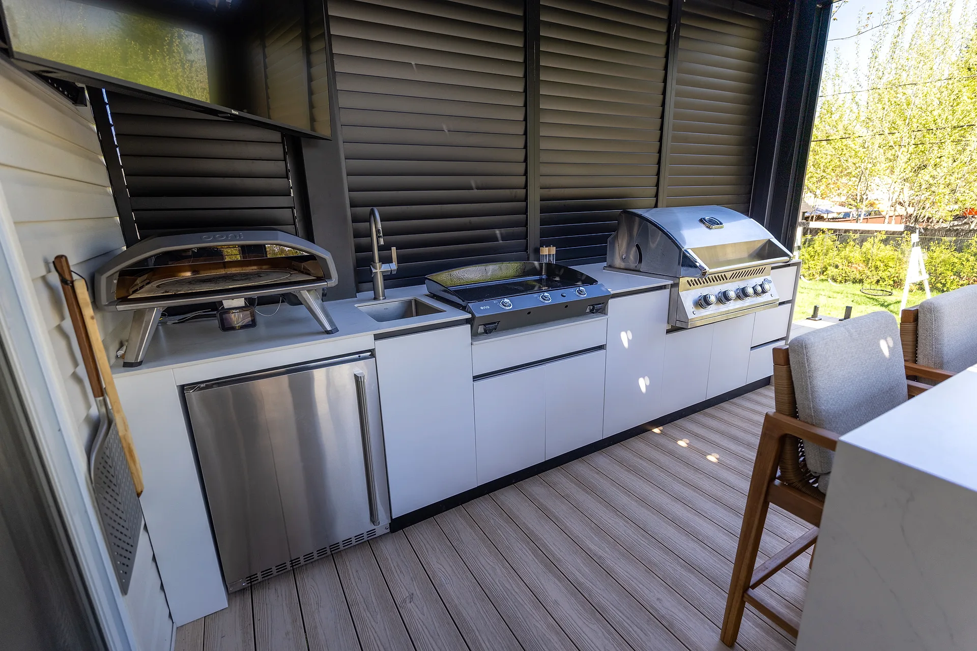 Linear outdoor kitchen in Mascouche under a bioclimatic pergola, with pizza oven, Eno plancha, and Napoléon BBQ