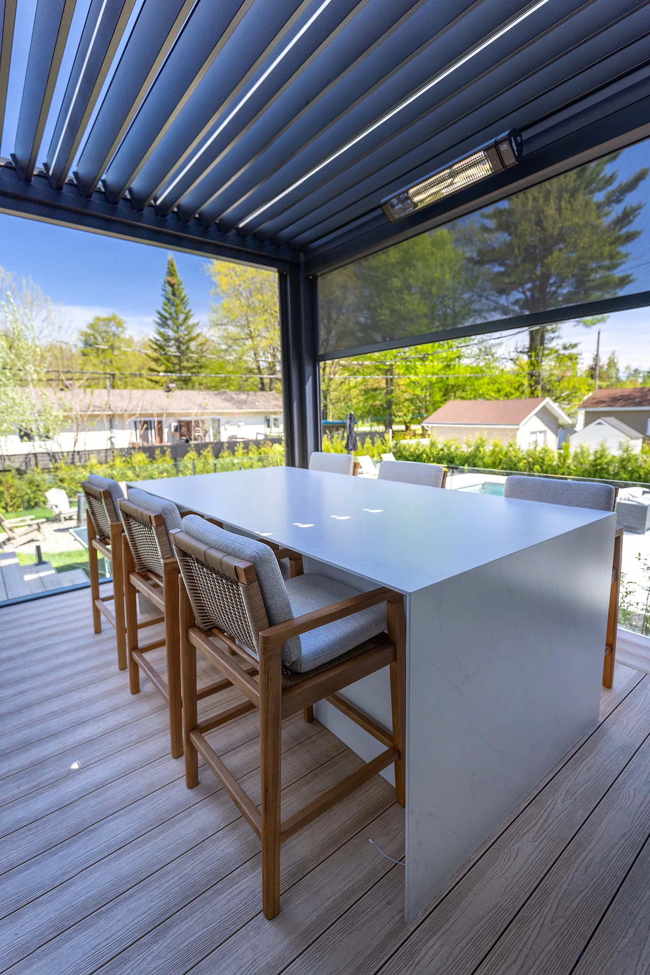 Outdoor kitchen dining area under a bioclimatic pergola, overlooking the landscaped yard