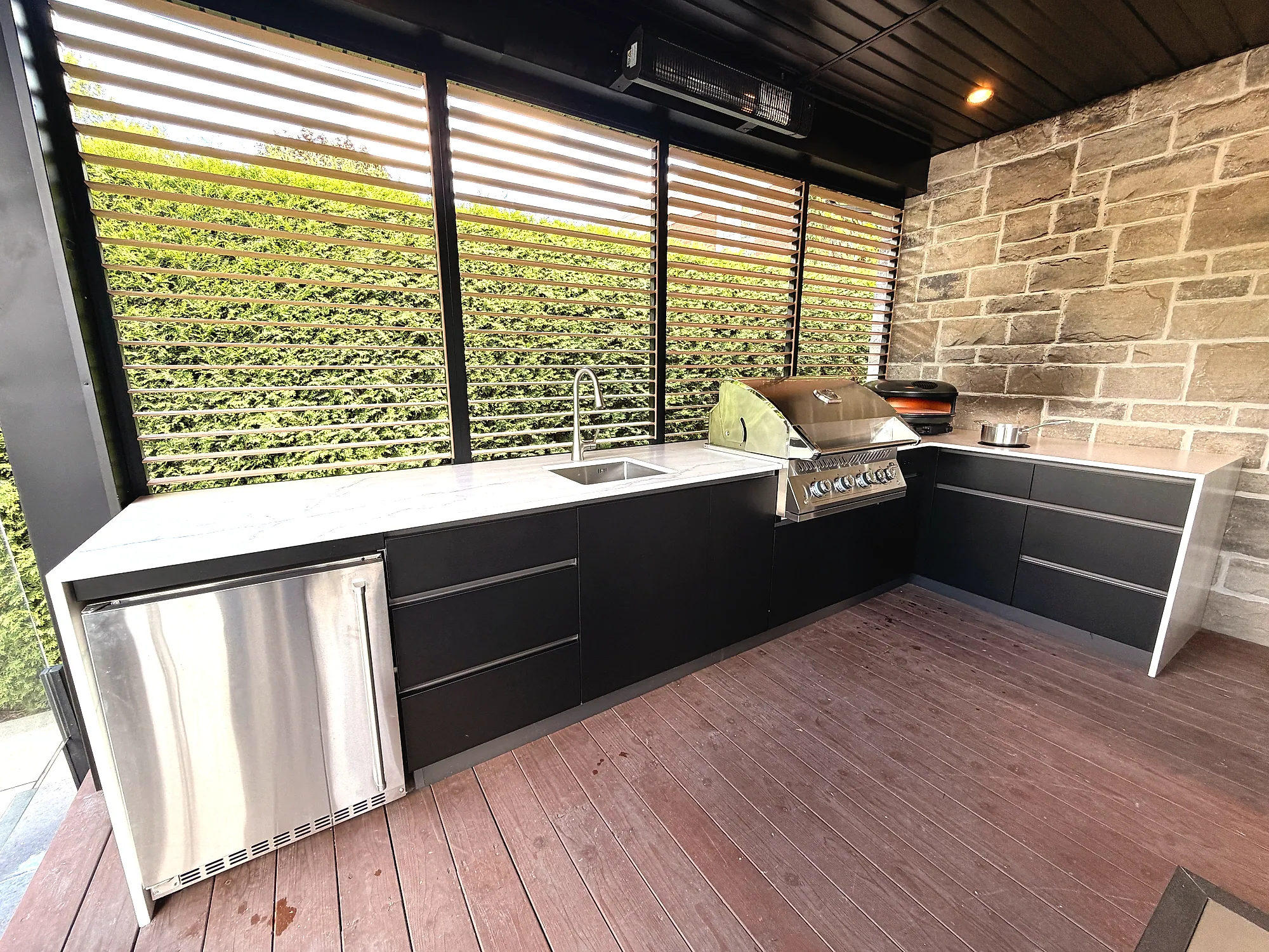 Vue d’ensemble de la cuisine extérieure en L avec réfrigérateur sous comptoir, évier et mur d’intimité à lamelles orientables, projet Mercier à Saint-Augustin-de-Desmaures