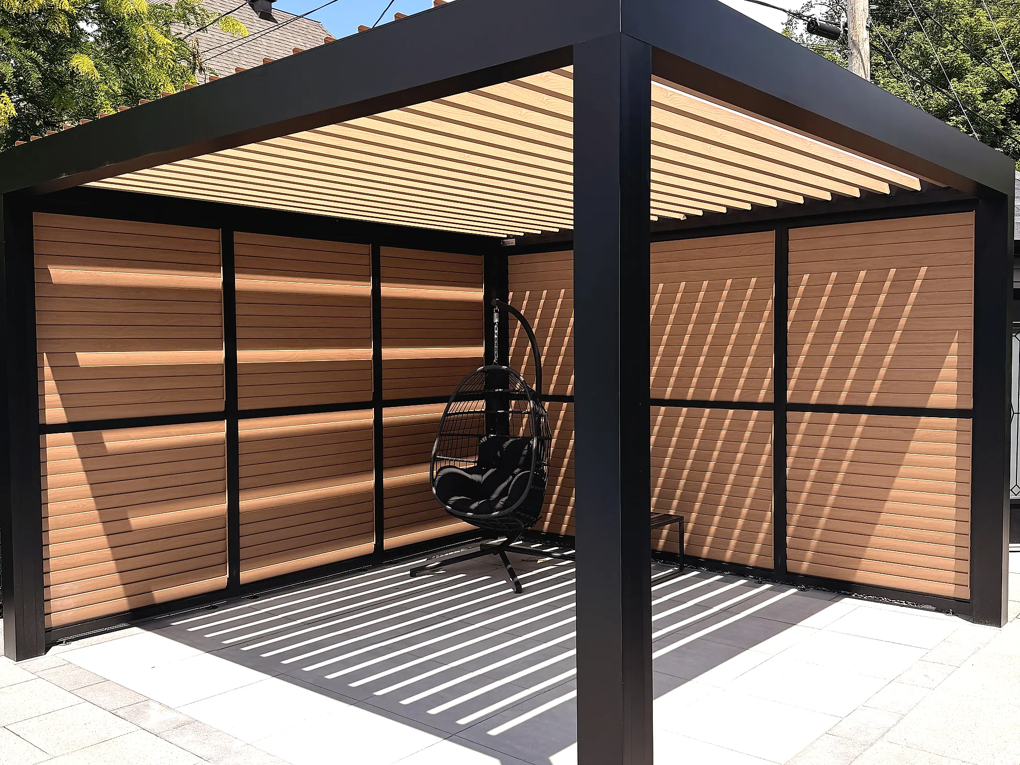 Pergola bioclimatique autoportante Pergolas Signature à lames orientables fini bois sur terrasse pavée, seconde zone de détente du projet Mercier