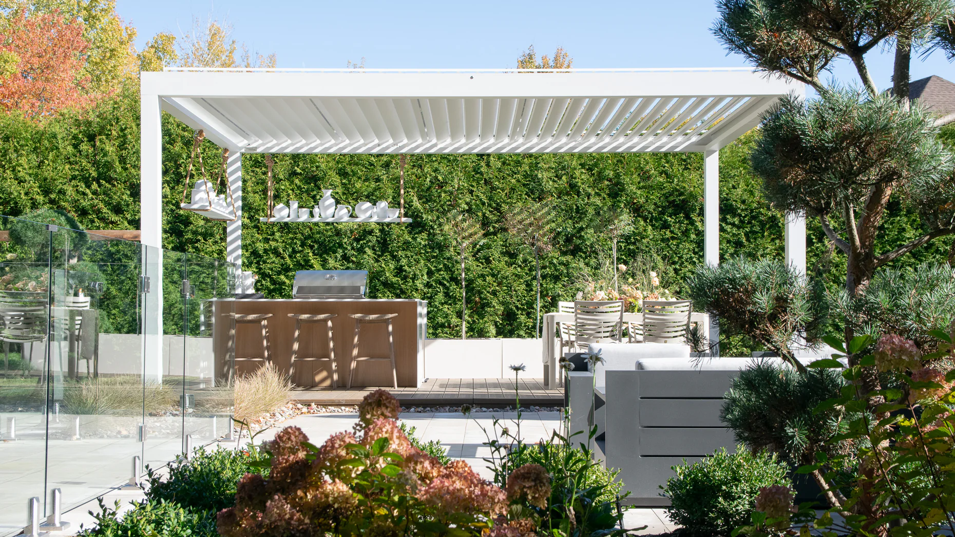Outdoor kitchen under a white bioclimatic pergola with bar seating and built-in BBQ in Blainville
